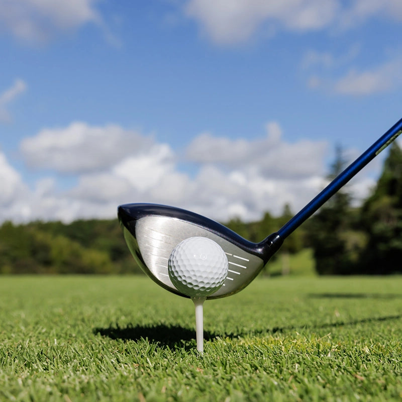 Golfball auf Golftee und Golfschläger dahinter auf der Rasenfläche