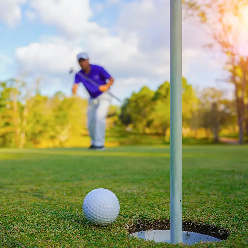 Golfer steht hinter Golfball und Golffahne mit Loch