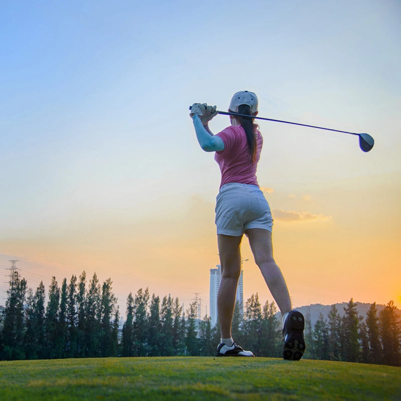 Frau spielt Golf und hält Schläger hinter dem Kopf bei Sonnenuntergang
